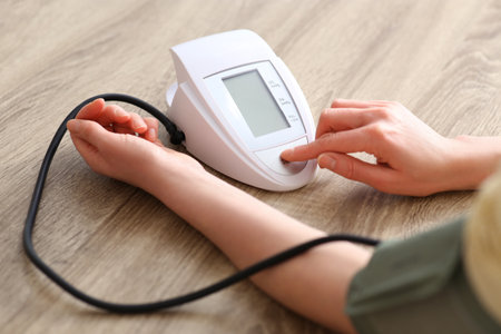 Woman checking blood pressure at wooden table indoors, closeupの写真素材
