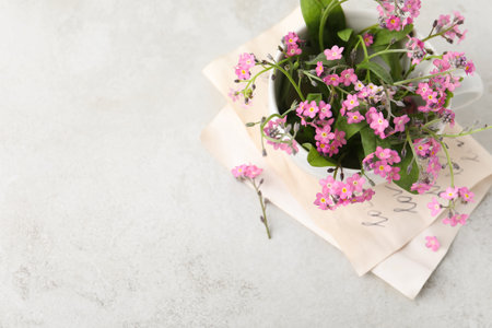 Beautiful pink forget-me-not flowers in cup on light stone table, top view. Space for textの写真素材