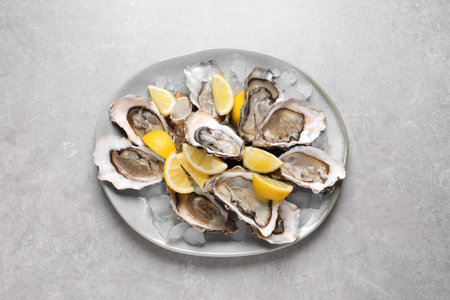 Fresh oysters with lemon and ice on gray table, top viewの写真素材