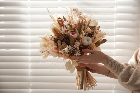 Woman holding beautiful dried flower bouquet near window at home, closeupの写真素材