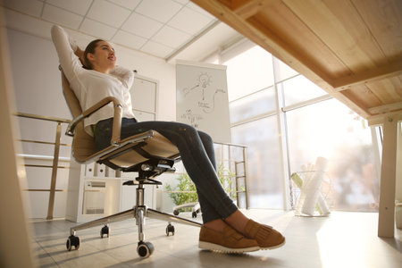 Young woman relaxing in office chair at workplace, low angle viewの写真素材