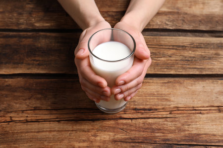 Woman holding glass of milk at wooden table, closeupの写真素材