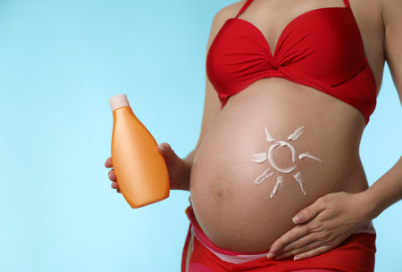 Young pregnant woman with sun protection cream on light blue background, closeupの写真素材
