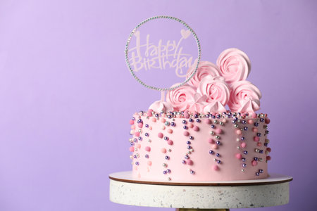 Beautifully decorated birthday cake on stand against violet background, space for textの写真素材