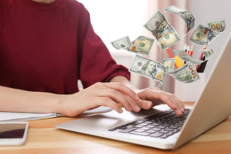 Making money online. Closeup view of woman using laptop at table and flying dollarsの写真素材