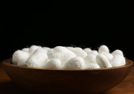 White silk cocoons in bowl on wooden table, closeupの写真素材