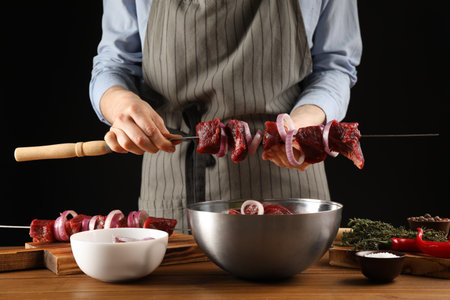 Woman stringing marinated meat on skewer at wooden table, closeupの写真素材