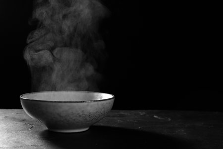 Bowl with white steam on black slate table. Space for textの写真素材