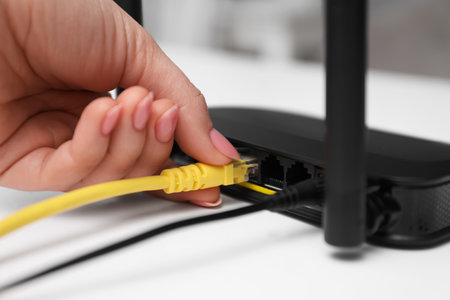 Woman connecting cable to router at white table, closeup. wireless internet communicationの写真素材