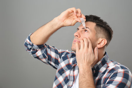 Man using eye drops on gray backgroundの写真素材