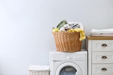 Wicker basket with dirty laundry on washing machine indoors, space for textの写真素材