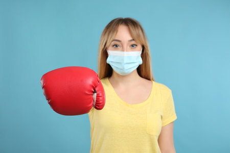 Woman with protective mask and boxing gloves on light blue background. Strong immunity conceptの写真素材