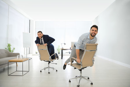 Happy office employees riding chairs at workplaceの写真素材