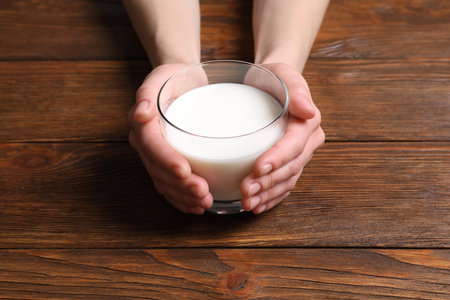 Woman holding glass of milk at wooden table, closeupの写真素材