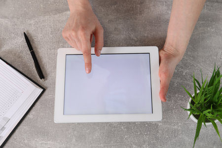 Woman using tablet with blank screen at gray stone table, top view. Space for text
