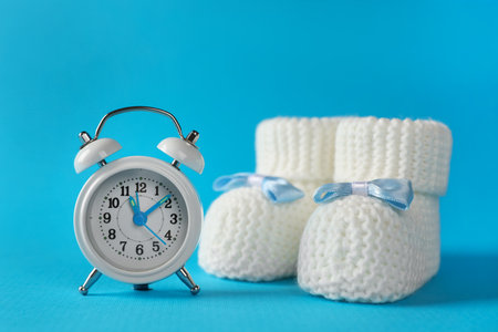 Alarm clock and baby booties on light blue background. Time to give birthの写真素材