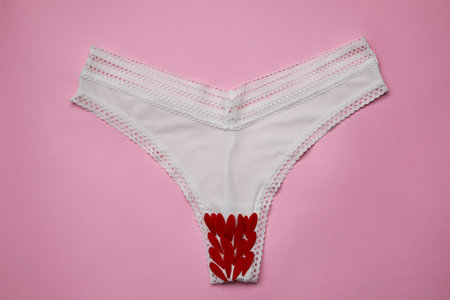 Woman's panties with red flower petals on pink background, top viewの写真素材