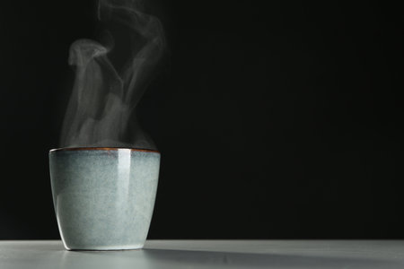 Mug with steam on table against black background. Space for textの写真素材