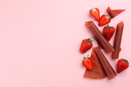Delicious fruit leather rolls and strawberries on pink background, flat lay. Space for textの写真素材