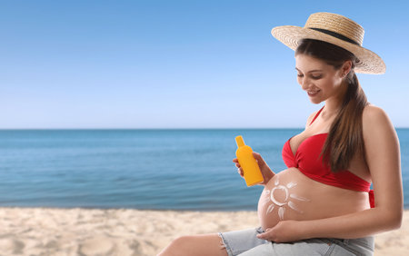 Young pregnant woman with sun protection cream on the beach. Space for textの写真素材
