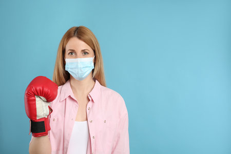 Woman with protective mask and boxing gloves on light blue background, space for text. Strong immunity conceptの写真素材
