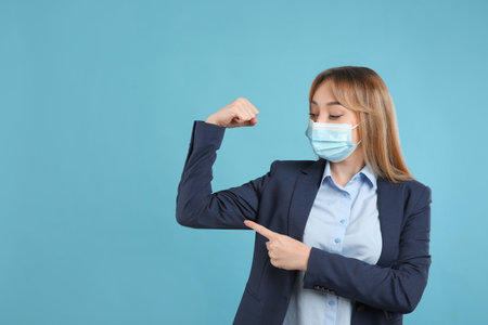 Businesswoman with protective mask showing muscles on light blue background, space for text. Strong immunity conceptの写真素材