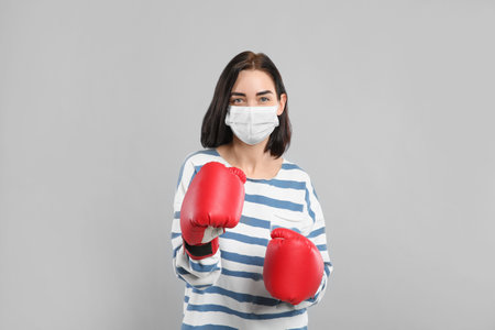 Woman with protective mask and boxing gloves on light gray background. Strong immunity conceptの写真素材