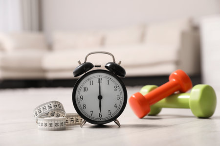 Alarm clock, measuring tape and dumbbells on wooden floor indoors. morning exerciseの写真素材