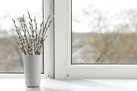 Beautiful pussy willow branches in vase on window sill indoors, space for textの写真素材