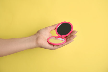 Woman holding pink cosmetic pocket mirror on yellow background, closeupの写真素材