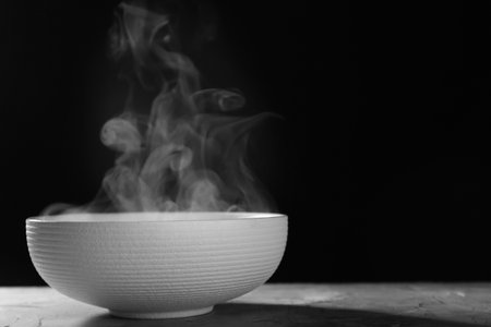 Bowl with steam on table against black background. Space for textの写真素材