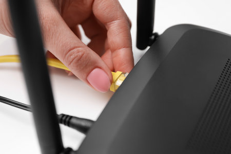 Woman connecting cable to router at white table, closeup. wireless internet communicationの写真素材