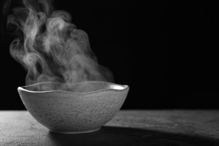 Bowl with steam on table against black background. Space for textの写真素材