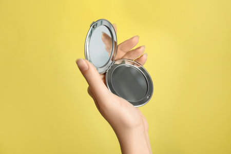 Woman holding metal cosmetic pocket mirror on yellow background, closeupの写真素材