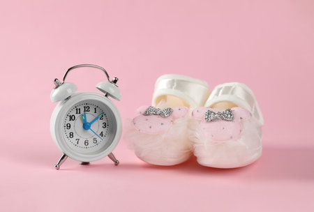 Alarm clock and baby booties on pink background. Time to give birthの写真素材