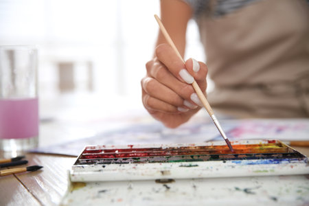 Young woman drawing with watercolors at table indoors, closeup. Space for textの写真素材