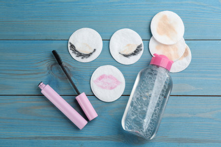 Dirty cotton pads, mascara and micellar cleansing water on blue wooden background, flat layの写真素材