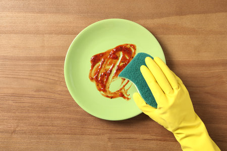 Woman washing dirty plate on wooden table, top viewの写真素材