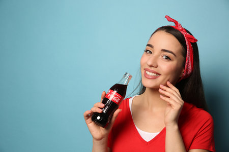 MYKOLAIV, UKRAINE - JANUARY 27, 2021: Young woman holding bottle of Coca-Cola on light blue background. Space for textのeditorial素材