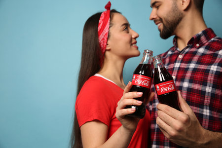 MYKOLAIV, UKRAINE - JANUARY 27, 2021: Young couple holding bottles of Coca-Cola against light blue background, closeup. Space for textのeditorial素材