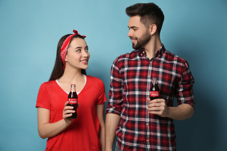 MYKOLAIV, UKRAINE - JANUARY 27, 2021: Young couple holding bottles of Coca-Cola on light blue...