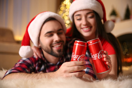 MYKOLAIV, UKRAINE - JANUARY 27, 2021: Young couple holding cans of Coca-Cola at home, focus on hands. christmas atmosphereのeditorial素材