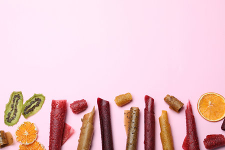 Delicious fruit leather rolls on pink background, flat lay. Space for text