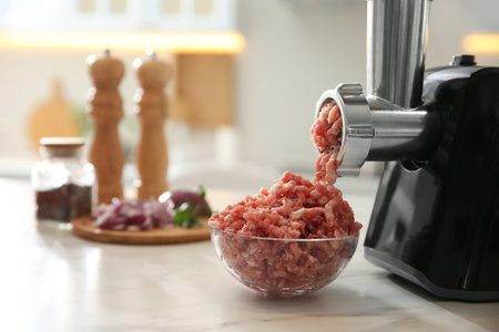Modern meat grinder and products on white marble table in kitchen. Space for text