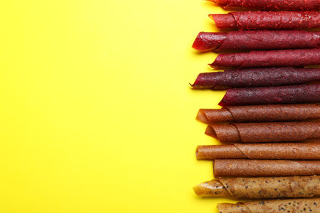 Delicious fruit leather rolls on yellow background, flat lay. Space for textの写真素材