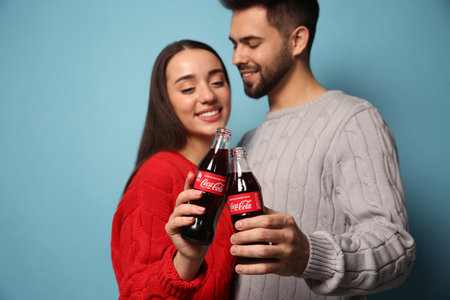 MYKOLAIV, UKRAINE - JANUARY 27, 2021: Young couple holding bottles of Coca-Cola against light blue background, focus on handsのeditorial素材