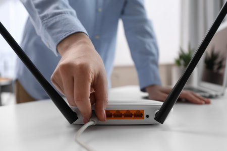 Woman connecting cable to router at white table indoors, closeup. wireless internet communicationの写真素材