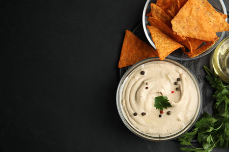 Delicious hummus with nachos and parsley on black table, top view. Space for textの写真素材