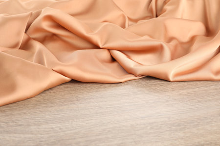 Beautiful delicate peach silk on wooden table, space for textの写真素材