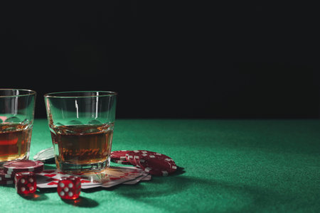 Casino chips, playing cards, dice and whiskey on green table, space for text